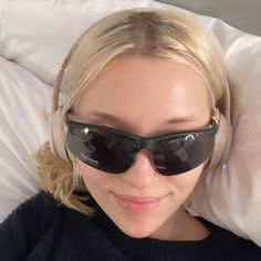 a woman laying in bed wearing sunglasses and headphones