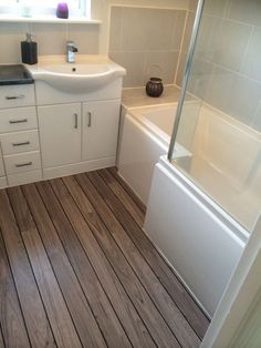 a bathroom with wood flooring and white fixtures, including a sink, bathtub, shower stall and window