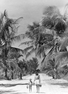 an old black and white photo of two people walking down a beach with palm trees