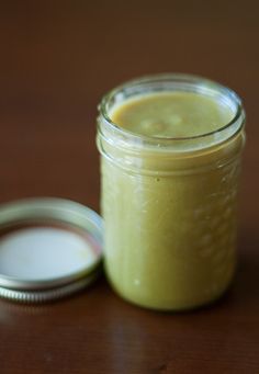 a glass jar filled with yellow liquid sitting on top of a wooden table next to a container