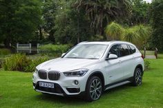 a white bmw suv parked on top of a lush green field