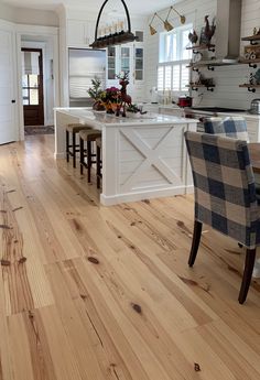 a kitchen with white walls and wooden floors has an island in the middle that is surrounded by chairs