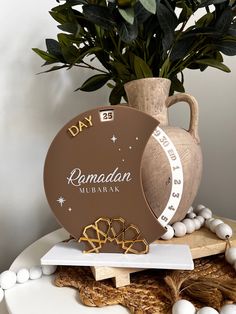 a white table topped with a vase filled with green leaves and beads next to a sign that reads ramadan mubarak