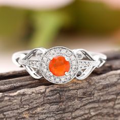 an orange and white diamond ring sitting on top of a piece of tree bark with flowers in the background