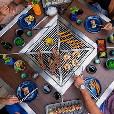 people sitting at a table with food and chopsticks in front of the grill