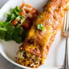 a white plate topped with an enchilada next to a salad and fork