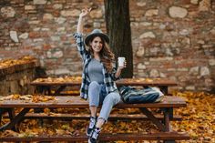 a woman is sitting on a bench with her arms in the air while holding a coffee cup