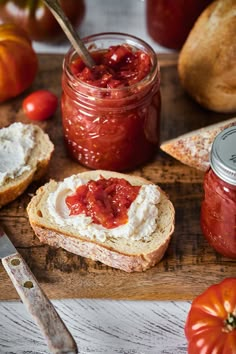 there is a jar of jam and bread on the cutting board with tomatoes in the background