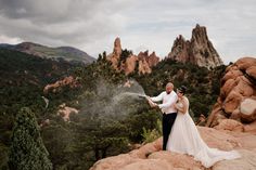 a bride and groom standing on top of a rock formation with mountains in the background