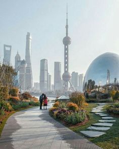 two people walking down a path in front of a large cityscape with tall buildings