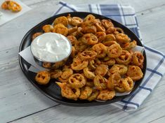 a black plate topped with onion rings next to a small bowl of ranch dressing on a blue and white checkered napkin