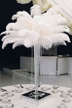 a white table topped with a tall vase filled with feathers and silver place settings on top of it