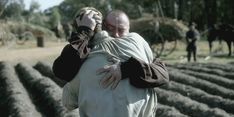 an older man is hugging another old man in the middle of a plowed field