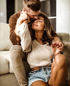 a man and woman are sitting on a couch together, one is kissing the other's forehead