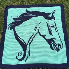 a crocheted blanket with a horse on it in the middle of some grass