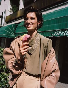 a woman holding an ice cream cone in her right hand and smiling at the camera