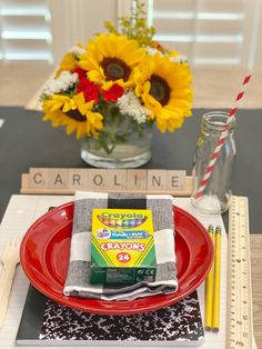 a place setting with sunflowers in a vase and napkin on a red plate