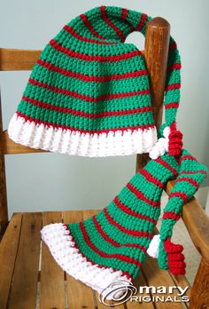 a green and red knitted hat sitting on top of a wooden chair next to a scarf