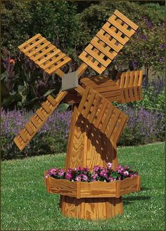 a wooden windmill sitting on top of a lush green field next to purple and white flowers