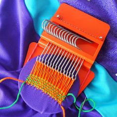 an orange loom is sitting on top of purple material and it's colorful