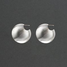 Named for the goddess of war, these shield like vessel earrings are powerful and the domed earrings are distinctly feminine. 1 1/2" in diameter and 1/2" wide the earrings nest close to your earlobe. The hollow forms are lightweight and a delight to wear. There is a mirror image texture detail that elevates the design. One side of the earring is high polish and the other has a soft matte texture. Big and bold, they're sure to make you feel invincible out in the world. FORM Collection Modern Silver Semi-circle Jewelry, Elegant Hand Forged Circle Earrings, Silver Sphere Earrings For Pierced Ears, Pierced Sphere Sterling Silver Earrings, Pierced Sterling Silver Sphere Earrings, Sterling Silver Round Wrap Earrings, Unique Round Earrings With Polished Finish, Silver Sphere Metal Earrings, Silver Round Earrings As Gift