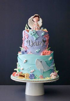 there is a blue cake with an image of a mermaid on top and under it