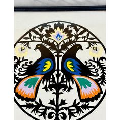 two colorful birds sitting on top of a white and black wall hanging from a metal frame