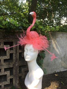 a white mannequin head with pink feathers and a flamingo on the top