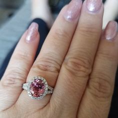 a close up of a person's hand holding a ring with a pink diamond