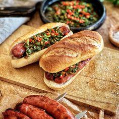 two hot dogs on buns with toppings next to a bowl of vegetables and bread