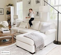 a person jumping up into the air in a living room with white furniture and pictures on the walls