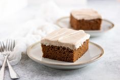 two slices of carrot cake with frosting on white plates next to silverware and napkins