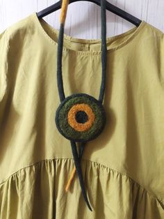 a green dress with an orange and yellow eyeball on it's back hanging from a wooden hanger