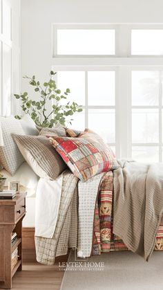 a bed with many pillows and blankets on top of it in front of a window