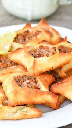 a white plate topped with pastries covered in meat and sauce next to a lemon wedge