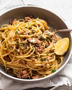 a bowl filled with pasta and meat on top of a white napkin next to a lemon wedge