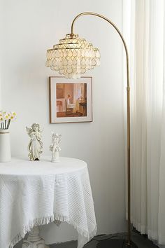 a white table with flowers on it next to a painting and a lamp in the corner