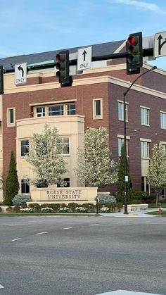 a traffic light sitting in front of a large building with trees on the side of it