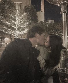 a man and woman kissing in front of a street light with christmas lights behind them