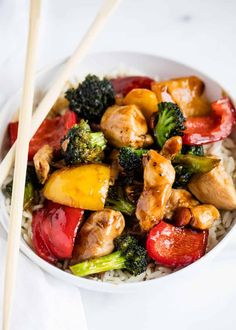 a white bowl filled with chicken, broccoli and peppers next to chopsticks