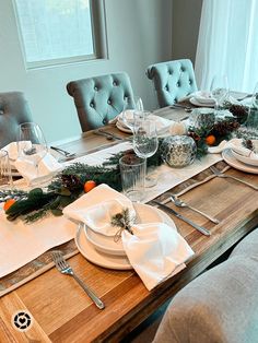 the table is set for christmas dinner with silverware and napkins on it, along with greenery