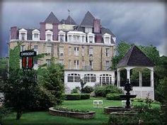 a large building sitting next to a lush green park filled with flowers and trees on a cloudy day