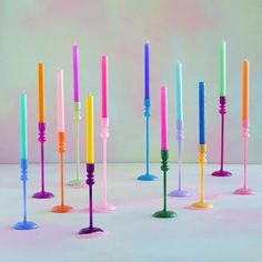 many different colored candles are lined up in a row on a table with pink and blue background