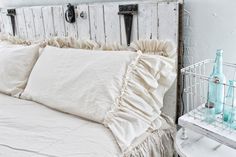 a white bed with ruffled pillows and bottles on the headboard next to it