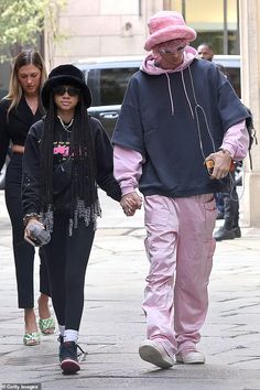 a man and woman walking down the street holding hands while wearing pink pants, black sweatshirts and matching hats