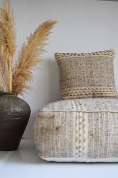 two vases with dried grass in them next to a chair and pillow on the floor