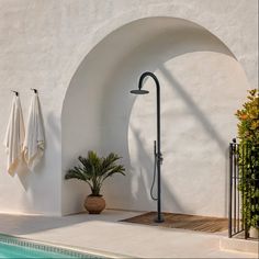 an outdoor shower next to a pool with towels hanging on the wall and potted plants