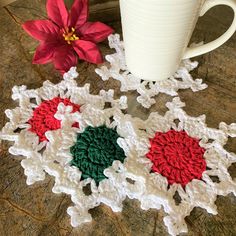 a crocheted snowflake next to a coffee cup on a table with a poinsetti in the background