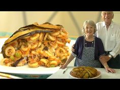 two people standing in front of a large pile of food on a white plate next to a cake