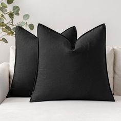 two black pillows sitting on top of a white couch next to a potted plant